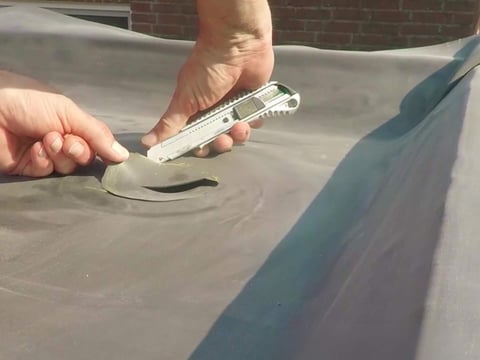 Snijdt een EPDM dakfolie met de hand met een cutter voor een nauwkeurige pasvorm tijdens de installatie van het dak