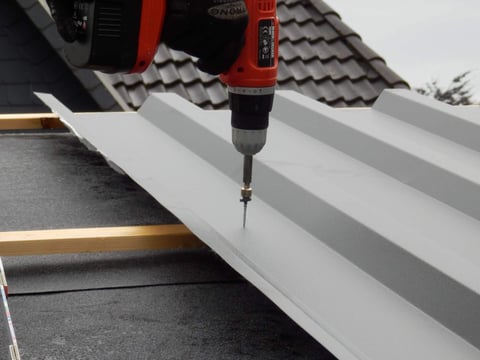 Een nokplaat monteren met een accuschroevendraaier op een trapeziumvormig plaatstalen dak