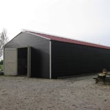 Groot gebouw met donkere gevel en rood dak, met lichtplaten in de daknok