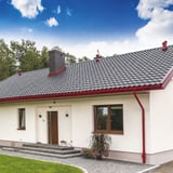 Huis met kersrode stalen dakgoten en regenpijpen van Niagara onder een blauwe lucht