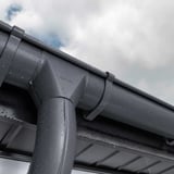 Niagara grafietgrijze dakgoot met regenpijp en waterdruppels op een bewolkte dag
