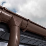 Chocoladebruine Niagara dakgoot met waterdruppels na regen, gemonteerd aan een dakrand
