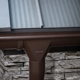 Detail van chocoladebruine Niagara dakgoot met uitloop op een stenen muur, dak met profielplaten