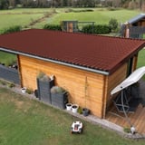 Dakpanplaat aluminium 0,70 mm roodbruin op het dak van een houten schuur met terras en robotmaaier
