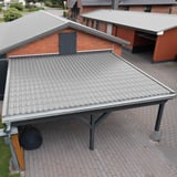 Dakpanplaat 2/1060 aluminium RAL9007 op een carportdak, ernaast een gebouw met rood pannendak
