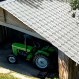 Dakpanplaat EUROPA lichtgrijs 0,50 mm op een afdak met groene tractor