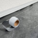 Dak reparatieband, grijze EPDM-band op rol op donker dakoppervlak, installatie op lichte muur