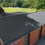 Damwandplaat 35/207 antracietgrijs als dak op een bakstenen gebouw naast een sportveld
