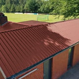 Damwandplaat 35/207, Roodbruin (RAL 8012) op een gebouw naast een sportveld
