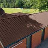 Damwandplaat 35/207, Chocoladebruin, als dak op een gebouw naast een sportveld