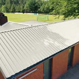 Damwandplaat 35/207 dak, Grijswit, gemonteerd op een lang gebouw met rode bakstenen gevel