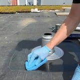 Montage EPDM activering: Hand met blauwe handschoen brengt zwarte oplosmiddel aan op EPDM-dakbaan