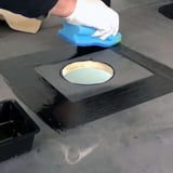 Montage van EPDM activering: Een hand met witte handschoen brengt zwarte vloeistof aan rond een dakafvoer