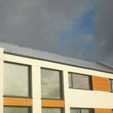 Modern gebouw met staande felsplaat PD-510-S Lichtgrijs (RAL 7035) dak onder bewolkte hemel