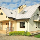 Huis met staande naadplaat PD-510-S dak in zuiverwit, met dakramen en schoorstenen, blauwe lucht