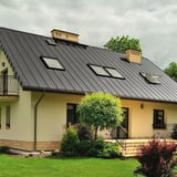 Staande felsplaat PD-510-S vlak, grijs aluminiumkleurig, op een woonhuis met meerdere dakramen