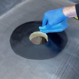 Hand met blauwe handschoen reinigt de zwarte EPDM dakbaan rond de garantie-gully