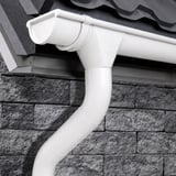 Witte dakgoot en regenpijp van Niagara, gemonteerd aan een huis met bakstenen muur en dakpannen