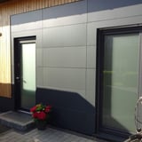Entree van een huis met donkergrijze HPL plaat gevelbekleding en houten elementen