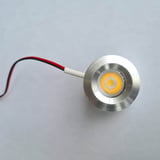 Detail van een enkele ronde LED lamp van blank aluminium, ingeschakeld met warmwit licht