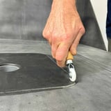 Hand leidt de metalen hoekroller met wit nylon wiel op donkere dakbedekking