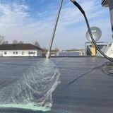 DACHPROTECT Spraybond 100 oppervlakte lijm wordt op een zwarte dakbaan gespoten
