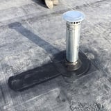 Detail van een geïnstalleerde zwarte EPDM buismanchet rond een ventilatiepijp op een plat dak
