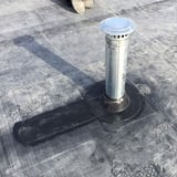 Detail van een zwarte EPDM buismanchet rond een metalen buis op een plat dak