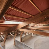 Binnenkant van een dakconstructie met houten balken en terracotta golfplaten