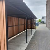 Donkergrijze golfplaten van Stabipol op een lange overkapping met houten wanden, verlegd