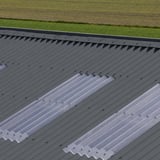 Detail van donkergrijze golfplaten met transparante lichtplaten op een dak
