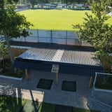 Bovenaanzicht van overkapping met donkergrijze golfplaten dak en lichtplaten bij sportveld