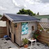Donkergrijze golfplaten op het dak van een houten tuinhuisje, verlegd met dakgoot