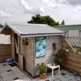 Lichtgrijze Stabipol golfplaten van polyester als dakbedekking op een houten tuinhuisje