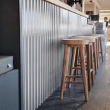 Lichtgrijze Stabipol golfplaten van polyester als wandbekleding in een interieur met houten krukken