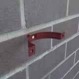 Kersrode stalen regenpijpbeugel gemonteerd op een bakstenen muur, met zichtbare schroef