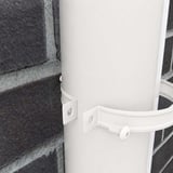 Detail van zuiverwitte (RAL 9010) regenpijpbeugel gemonteerd op een regenpijp aan een bakstenen muur
