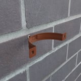 Enkele koperbruine (RAL 8004) valbuisklem gemonteerd aan een bakstenen muur, detail van bevestiging