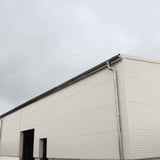 Sandwichpaneel Wall 1100 80, Grijswit, als gevel van een gebouw met dakgoot en regenpijp