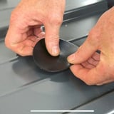 Handen plaatsen een zwarte EPDM schroef reparatiepleister op een profielplaat