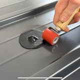 Hand rolt met een rode roller over een zwarte EPDM schroef reparatiepleister