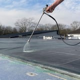 Spuitlans in gebruik op een plat dak, een hand houdt de lans vast