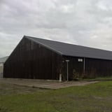 Grote schuur met zwart dak van golfplaten en donkere houten wanden onder bewolkte hemel
