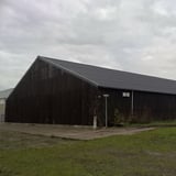 Grote donkere schuur met zwart golfplaten dak van vezelcement, bewolkte dag