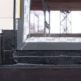 Detailaanzicht van een raamafdichting met zwarte vloeibare kunststof op een gebouwhoek