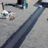 Plaatsing van het zwarte DACHPROTECT vorm- en afdekband van EPDM voor het afdichten van een daknaad
