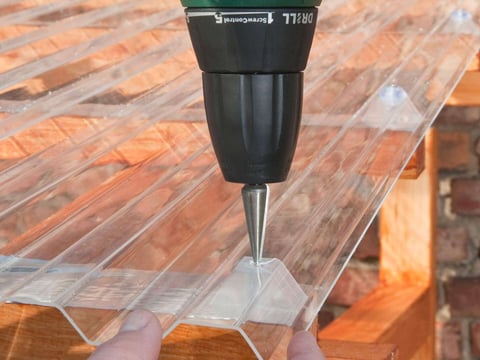 Handmatige installatie van transparante golfplaten met een accuboormachine op een houten dakspant, nauwkeurig en efficiënt doe-het-zelf-werk