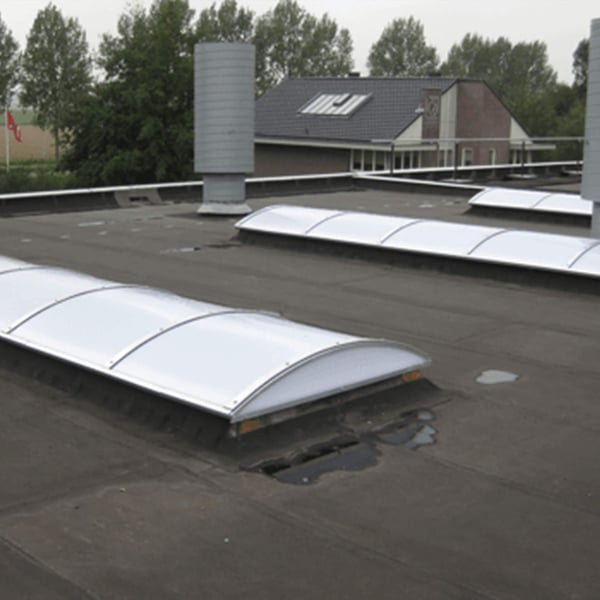 Twee Alumon lichtkoepels op een plat dak met ventilatiebuizen op de achtergrond