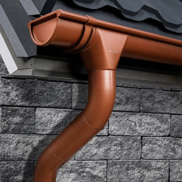 Koperbruine dakgoot en regenpijp van Niagara gemonteerd aan een huis met stenen muur en dakpannen