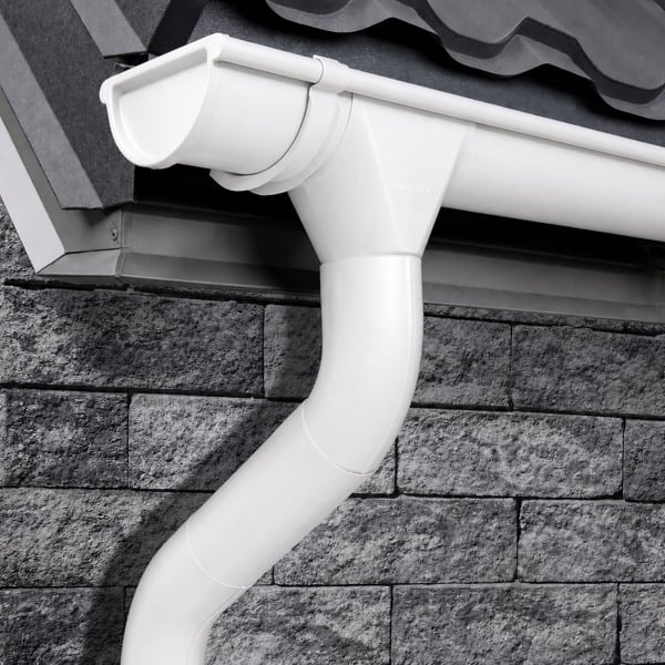 Geïnstalleerde zuiverwitte Niagara dakgoot en regenpijp op een huis met grijze dakpannen en bakstenen muur